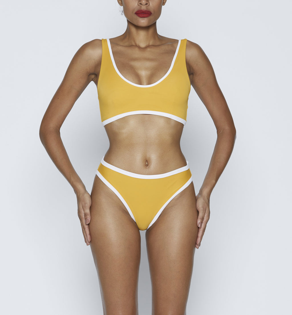 Swimwear Top. Pullover bikini sport bra style top  in vintage yellow with White contrast binding outline. Bikini bottom. Mid to High Waisted Swimwear bottom in yellow vintage with White binding outline. Medium to full coverage bikini bottom. High Legs swimsuit bottom. Check out our fashion boutique swimsuit online shop. supper soft fabric Nylon/spandex. sport bikini