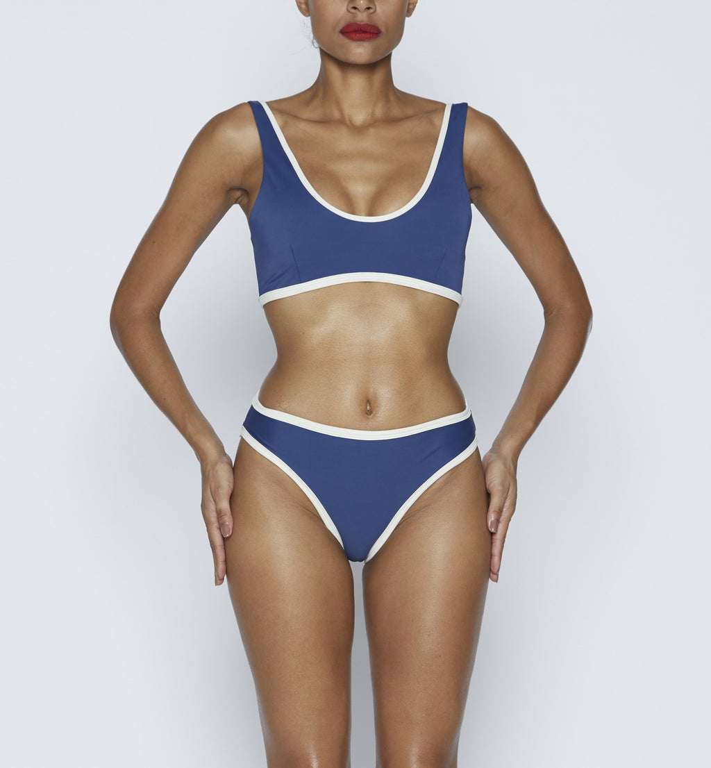 Swimwear Top. Pullover bikini sport bra style top  in dark Blue with Off White contrast binding outline. Bikini bottom. Mid to High Waisted Swimwear bottom in Dark Blue with Off White. Medium to full coverage bikini bottom. High Legs swimsuit bottom. Check out our fashion boutique swimsuit online shop.